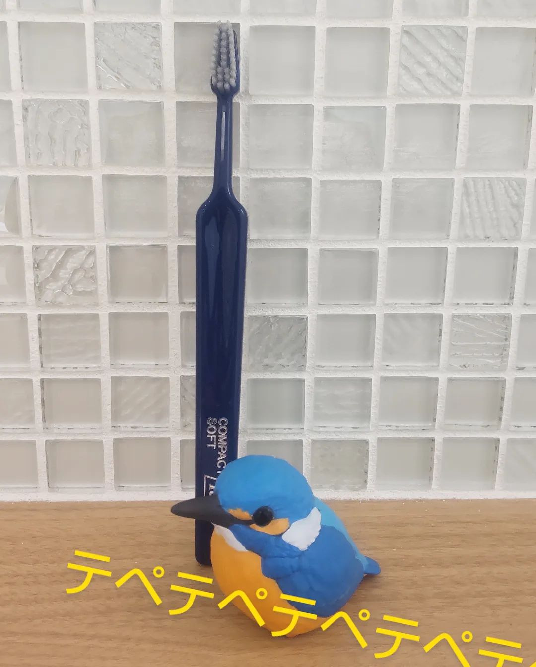 立てた紺色のTePe歯ブラシとカワセミの置物の写真